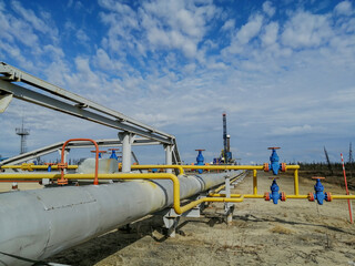 Pipeline fittings and manifold of producing gas wells in the field. Handwheels for high pressure valves. In the background, a drilling rig. Blurring distant objects.