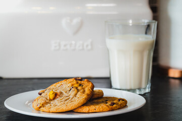 A plate of delicious and freshly baked warm chocolate chip cookies next to a cold glass of milk, ready to be enjoyed at any time of the day.