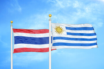 Thailand and Uruguay two flags on flagpoles and blue sky