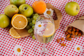 Fruit, nuts and a glass of water with lemon and chamomile flower is on the table.
