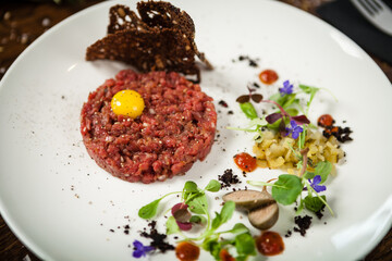 Fototapeta na wymiar Steak tartare. Horseradish creme, black bread, baguette chips on white plate. Delicious healthy raw meat food closeup served on a table for lunch in modern cuisine gourmet restaurant.