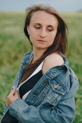 Beautiful young girl in a denim jacket in a green field of rye at sunset