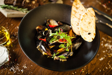 Blue mussels in white wine sauce in black bowl. Delicious healthy seafood closeup served on a table for lunch in modern cuisine gourmet restaurant
