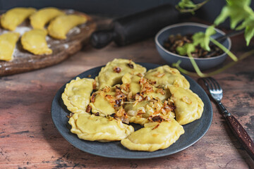 Homemade dumplings with potato and mushroom, blue plate, wooden rustic table at kitchen near window. Organic, healthy vegetable vegan food. Selective focus, copy space. 