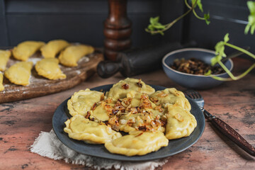 Homemade dumplings with potato and mushroom, blue plate, wooden rustic table at kitchen near window. Organic, healthy vegetable vegan food. Selective focus, copy space. 