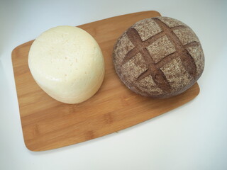 Head of cheese with a loaf of bread, baguette, buns with poppy seeds, close-up, wooden Board