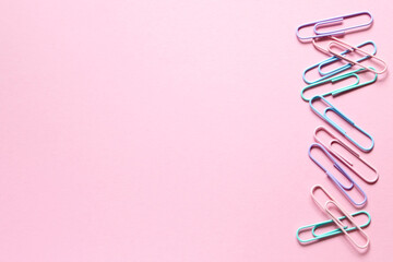 Gentle color paper clips laid out on a delicate pink background on one side in a row. Layout and flat lay with place for text. Concept back to school.