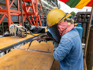 The welder is welding add joint a steel plate with process Flux Cored Arc Welding(FCAW) and dressed properly with personal protective equipment(PPE) for safety, at industrial factory.