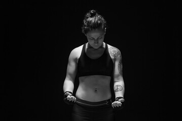 A young, female boxer with dark hair styled with a fade on one side, stands in contemplation of her next bout. 