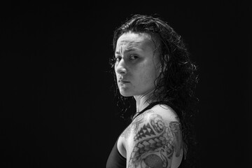 A young, female boxer with dark hair styled with a fade on one side, stands in contemplation of her next bout. 