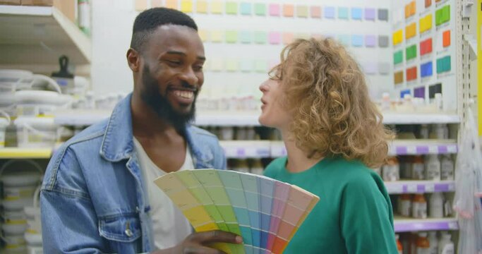Young smiling diverse couple choosing color for walls in hardware store