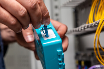 A man works with a blue fiber optical connector cleaner near a cabinet. Cleaning connectors close...