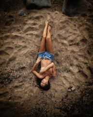 Summertime recreation concept. Beautiful young sexy woman with fit trained slim body wearing blue shorts lies on a beach. Fashion female model poses by the sea.