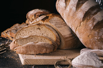 Assortment of baked bread and bread rolls on black table black background.