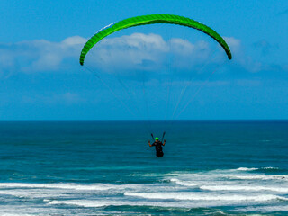 Para glider soars over the beach, waves and hills at Murawai Beach, Auckland, New Zealand