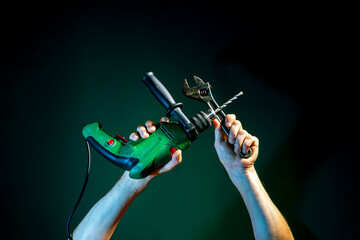 Raised Male hands holding spanners and a drill on a dark  background
