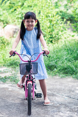 Fototapeta na wymiar Asian little girl riding her bicycle outside with smile and happy