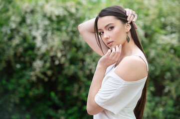 beautiful fashionable girl in stylish jewelry. The model poses in the street with flowering trees.