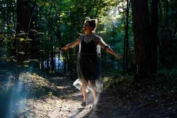 A girl in a beautiful dress dancing in the sunlight among the thickets of dense forest