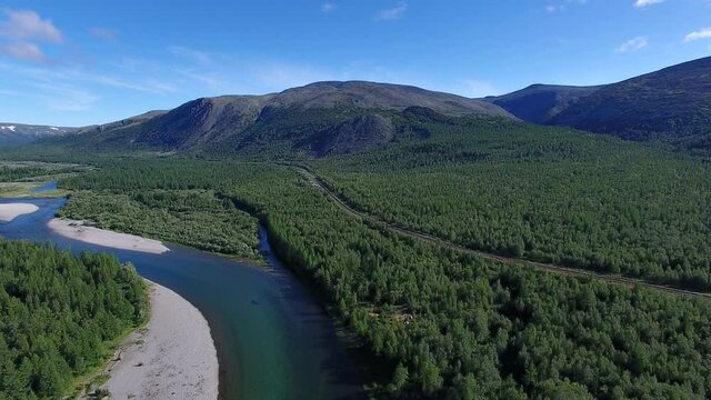 The camera flies over the valley of a mountain river. Along the river there is a railway, on the sides of the mountain