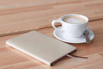White coffee cup and beige diary on a wooden background
