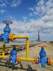 Fototapeta na wymiar Pipeline fittings and manifold of producing gas wells in the field. Handwheels for high pressure valves. In the background, a drilling rig. Blurring distant objects.