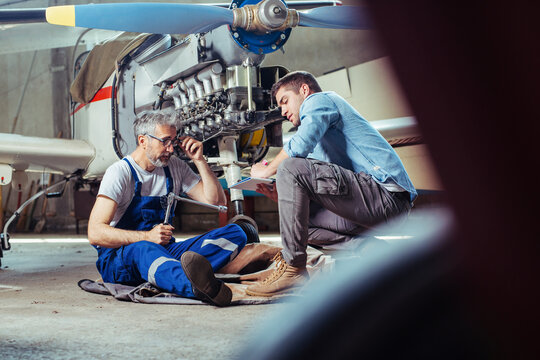 Aircraft Mechanics In The Hangar. Coworkers Repairing An Aircraft