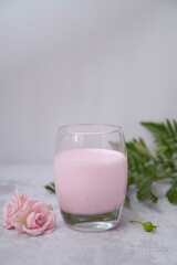 glass of pink milk and flowers on white background.