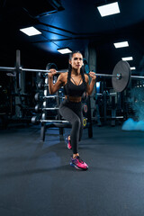 Fototapeta na wymiar Female bodybuilder doing lunges using barbell in gym.