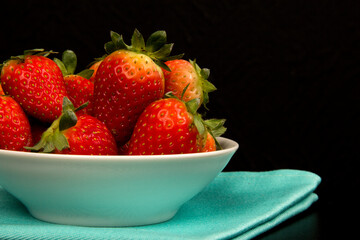Red fresh strawberry in a bowl on black background.