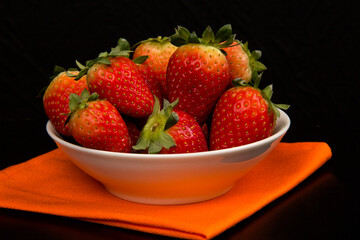 Red fresh strawberry in a bowl on black background.