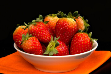 Red fresh strawberry in a bowl on black background.