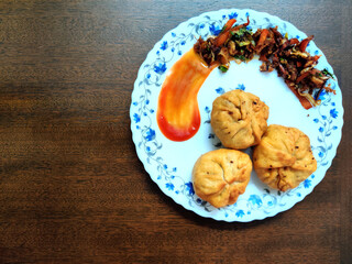 Three veg fried dumpling or momos with filling on the side decorated with red tomato ketchup served in a white plate on a wooden table top view