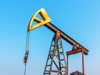 A Small private oil derrick pumps oil on the field. The old handicraft oil rig in the background of the creative industrial design.