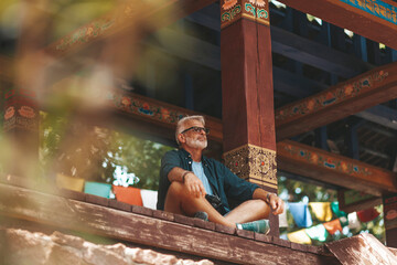 Senior man with beard rest in buddhist monastery. Elderly hiker has active journey. Exotic resort...