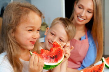 Sweet family, mother and her kids eating watermelon in their kitchen having fun