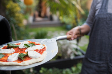 Woman cooking homemade pizza at pizza oven on patio