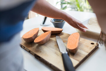 Woman slicing sweet potatoes on cutting board in kitchen