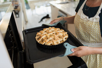 Woman removing fresh baked lattice apple pie from kitchen oven