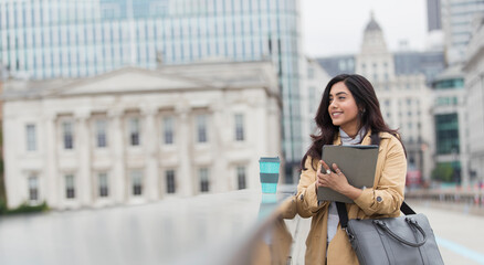 Ambitious businesswoman with digital tablet and coffee on city bridge