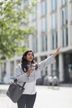 Woman with headphones and smart phone hailing crowdsourced taxi