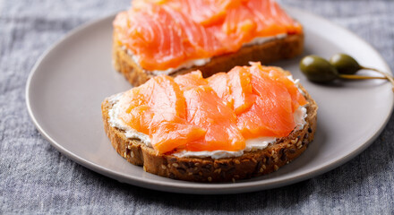 Sandwich, toast with smoked salmon and cream cheese on a plate. Grey background. Close up.