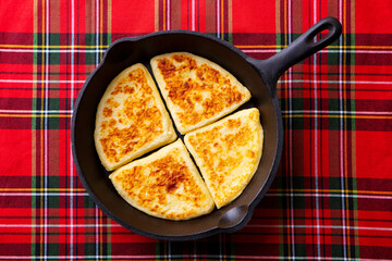 Traditional Scottish tattie potato scones in cast iron pan. Plaid fabric napkin background. Top...