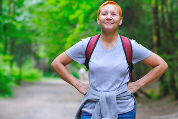 A smiling tourist girl stands on a forest path. A backpack is slung over his shoulders.