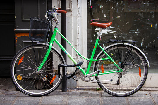 A green bicycle, one of the more popular modes of transportation in Paris, France, is chained to a pole outside an old building.