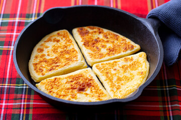 Traditional Scottish tattie potato scones in cast iron pan. Plaid fabric napkin background. Close up.