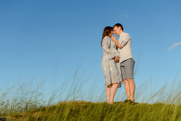 Happy young couple kissing on top of a mountain, with clear sky in the background. Happy family