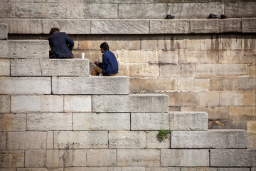 Obraz na płótnie Canvas Two men sit on stone steps by the River Seine enjoying a relaxing cup of coffee in Paris, France.