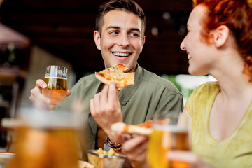 Happy couple talking while eating pizza and drinking beer in a pub.