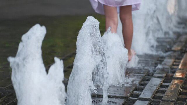 City pavement with fountains in a row. Little girl have fun, playing in a water streams at sunny summer day.